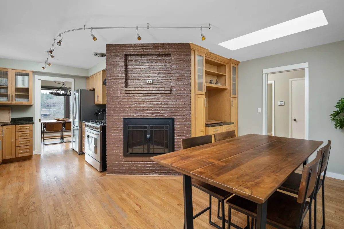 A cozy yet expansive open layout uniting the dining table, fireplace, and kitchen. The inviting fireplace and communal table set a scene for shared meals, conversation, and togetherness in a warm environment.
