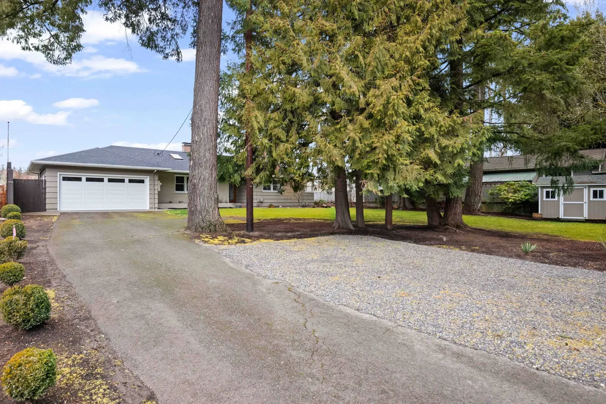 The exterior shot shows a spacious driveway framed by large, leafy trees and a glimpse of the garage. The natural surroundings reinforce a sense of seclusion and provide an inviting environment for outdoor relaxation and activities, such as enjoying morning coffee amidst nature or hosting gatherings.