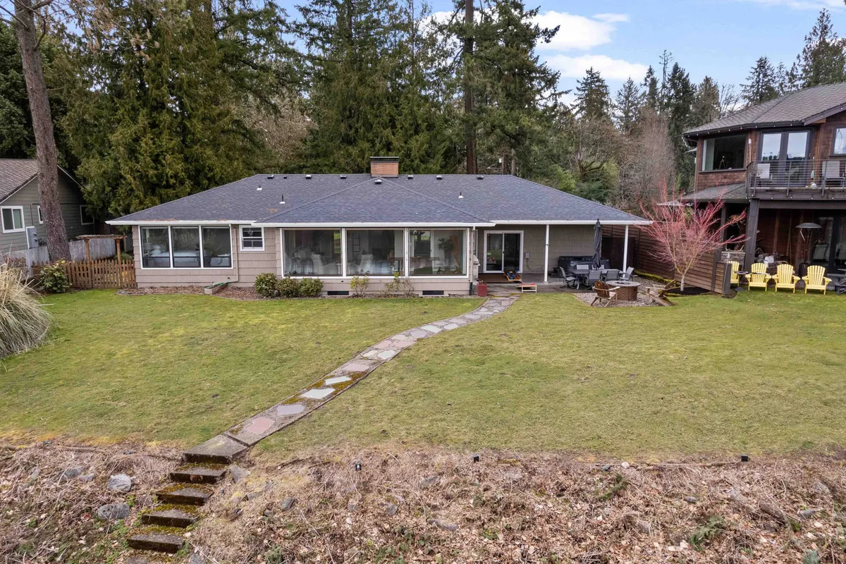 This image shows an expansive green lawn with a stone pathway, a seating area, and large windows looking out from the home. The inviting outdoor space is perfect for relaxation or playful moments with pets. The lush lawn offers plenty of space for dogs to roam under supervision.