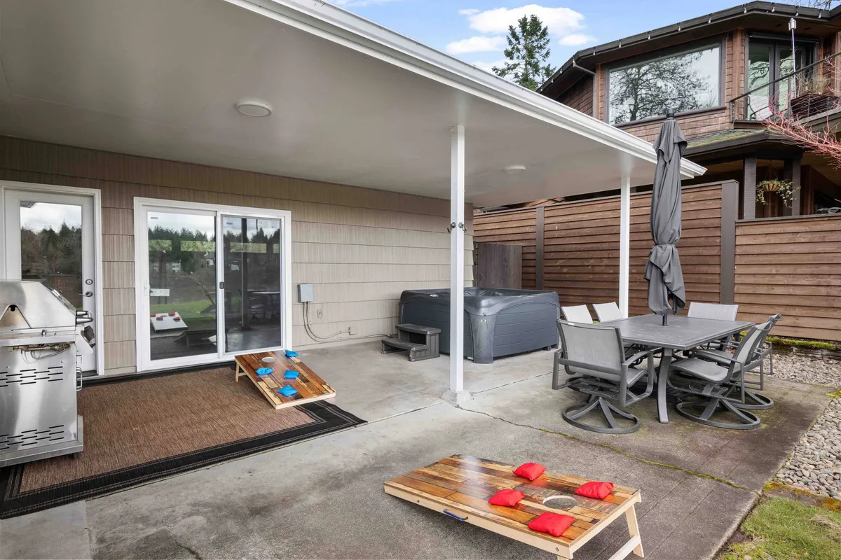 A vibrant outdoor space with a grill, bubbling hot tub, dining table, and a cornhole game set on the lawn. The overall vibe is playful and social, with plenty of room for gatherings and outdoor fun.